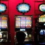 Three slot machines against a red wall in a casino.