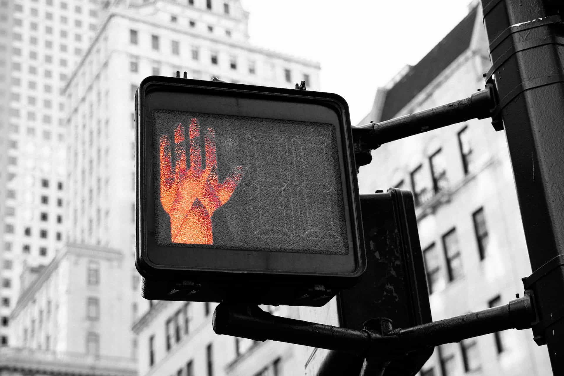 A stoplight displays a red hand to indicate stopping at a crosswalk.