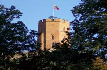 A brown building under a blue sky with a Lithuanian flag on top.