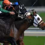 Two jockeys racing their horses head to head on a professional outdoor horse racing track.