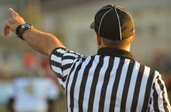 A referee in a striped uniform holds on his arm to signal to players.